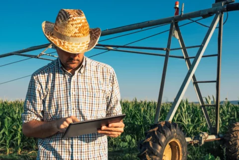 Farmer with electronic device and irrigation system behind him